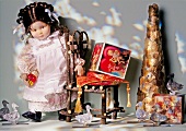 Doll with plaited hair standing beside small chair with Christmas decorations