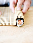 Sushi being rolled in bamboo mat with fingers