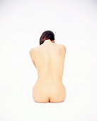 Rückenansicht einer nackten Frau, die auf dem Boden sitzt