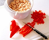 Bell pepper cut into small pieces on cutting board with white beans in bowl