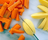 Peeled carrots and potatoes cut in bite sized pieces with knife, overhead view