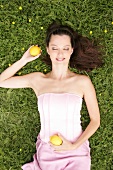 Relaxed woman lying on grass in meadow with lemons in hand, eyes closed