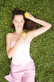Relaxed woman lying on grass in meadow with lemons in hand, eyes closed