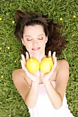 Pretty woman lying on meadow with eyes closed holding two lemons in cupped hands