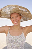 Portrait of cheerful woman wearing floral pattern dress and big straw hat on beach
