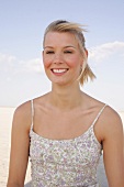 Portrait of beautiful woman in floral pattern dress standing on beach, smiling