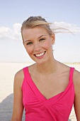 Jennifer Frau mit blonden Haaren trägt pinkes Top u. lacht, am Strand