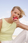 Woman sitting on beach and eating red apple
