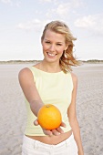 Jennifer Frau hält in einer Hand eine Orange, sie steht am Strand