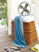 Fan with white cushion and blue towel on wicker basket
