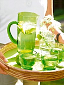 Green jug and glasses with water and lime on wicker tray