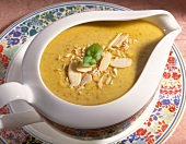 Curry sauce garnished with almonds in gravy boat kept on plate