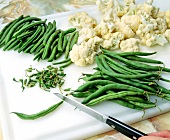 Cauliflower florets on cutting board and beans ends being cut with knife