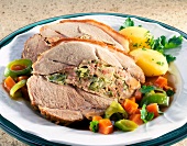 Stuffed pork shoulder with potatoes and vegetables on dish