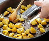 Close-up of cumin being sprinkled on fried potatoes in pan