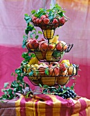 Different fresh fruits in tiered wire stand with tendrils on table