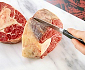 Raw bovine bone being cut in slices with knife on cutting board