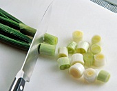 Close-up of spring onions being chopped with knife on cutting board