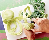 Kohlrabi being peeled with knife on cutting board