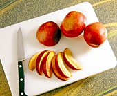 Peaches being cut into slices with kitchen knife on white chopping board