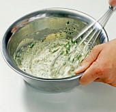 Chopped herbs being whisked with butter in bowl for preparation of herb butter, step 5