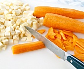 Close-up of celery cut into small pieces and carrots being sliced with knife