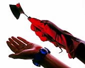 Close-up of woman's hand wearing red gloves and blue bracelets holding small brush