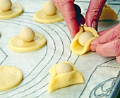 Close-up of woman's hands putting marzipan ball stuffing in the cut Christmas cookies