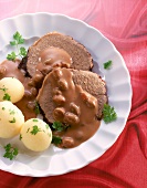 Close-up of sauerbraten with potato, raisin sauce and chervil in dish