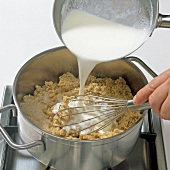 Hand pouring milk to mixture in pot, step 4
