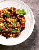 Chilli con carne with corn and basil leaves on plate