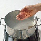 Hand putting dumplings in water in pot, step 7