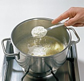 Hand adding flour to butter in pot, step 1