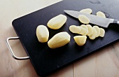 Potatoes being cut into thin slices with knife on chopping board