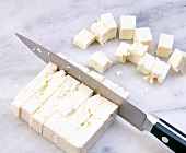 Cutting feta cheese into cubes with kitchen knife