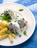 Close-up of hack dumplings in lemon sauce with potatoes, peas and lemon balm on plate