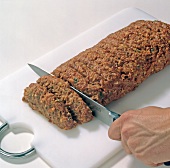 Close-up of hands cutting loaf of meat on chopping board