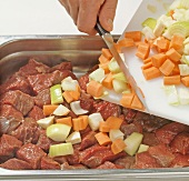 Close-up of vegetables being added to meat for preparing venison stew, step 2