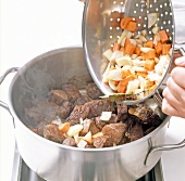 Close-up of adding vegetables to meat while preparing venison stew, step 9