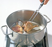 Close-up duck legs being fried in pot for preparation of wild duck, step 1