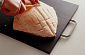 Roasted pork being carved diagonally with knife on wooden board, step 1