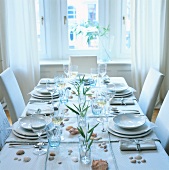 Gedeckter Tisch mit weißem Geschirr und Muscheldekoration, schlicht