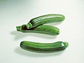 Three whole dark green zucchini on white background