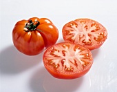 Close-up of whole and halved red ribbed beefsteak tomatoes on white background