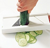 Close-up of zucchini being sliced with plastic slicer, step 1