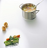 Poultry broth in pot with vegetables on white background, copy space