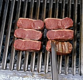 Six beef steaks on grill with tongs