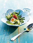 Herb salad with pancetta and egg in bowl on wooden surface