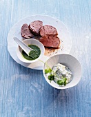 Fillet of beef on plate with two herb sauces in bowls