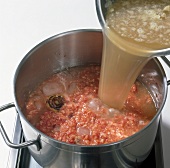 Pouring beef broth in pot with meat, siler root and ice cubes